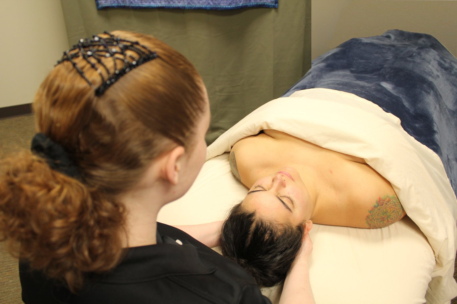 Emma working at the head of a massage table, hands cradling a client's neck