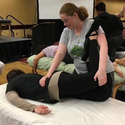 A table Thai stretch at a training, Emma guiding a client's leg through an assisted stretch